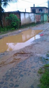 Segundo um leitor, no bairro do Ilhéus II, zona sul de Ilhéus, o trânsito dos pesados coletivos em uma das ruas, acarretou na formação de um desnível, que, crescendo gradativamente, já significa problemas aos moradores. A foto mostra a situação da via em dias de chuva.